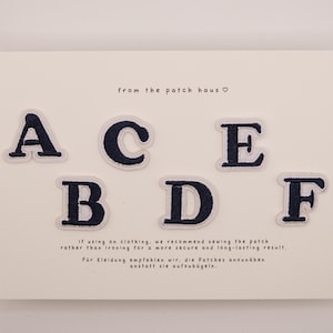 May include: Six dark navy blue embroidered letter patches featuring the letters A, B, C, D, E, and F arranged on a white card. The card includes the text from the patch haus and instructions for sewing the patches onto clothing items.