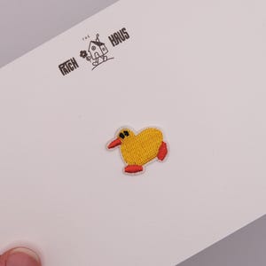 Op de afbeelding: Een kleine geborduurde patch met een geel vogelachtig figuurtje met een rode snavel en rode voetjes. De patch is bevestigd op een witte kaart bedrukt met de tekst THE PATCH HAUS en een kleine afbeelding van een huisje met een bloem.