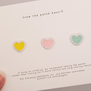 Könnte beinhalten: Drei kleine herzförmige Stickaufnäher in Gelb, Hellrosa und Mintgrün auf einer weißen Karte mit dem Text from the patch haus und Hinweisen zum Annähen der Aufnäher an Kleidung für ein sicheres und langlebiges Ergebnis.