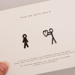 May include: Two black embroidered stick figure patches on a white card. One figure stands alone, while the other holds a white heart. The card features the text from the patch haus and instructions recommending sewing the patches onto clothing.