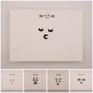 以下が含まれることがあります： 上部に黒い文字でPATCH HAUSと小さな家のアイコンが描かれた白い長方形のカード。中央には、長いまつげの閉じた目と小さな口の黒いグラフィックがあります。下部には、異なる表情をした4つの小さなバリエーションが並んでいます。
