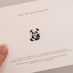May include: A small black and white embroidered panda patch centered on a white card. The card features the text from the patch haus and instructions in English and German regarding sewing the patch onto clothing for a secure result.