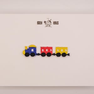 Peut inclure: Un écusson brodé thermocollant représentant un train coloré avec une locomotive bleue, un wagon central rouge et un wagon de queue jaune, tous dotés de roues noires. L'écusson est présenté sur une carte blanche avec le texte THE PATCH HAUS.