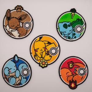 Puede incluir: Cinco parches bordados circulares con personajes durmiendo: un Eevee marrón, un Bulbasaur verde, un Pikachu amarillo, un Squirtle azul claro y un Charmander naranja. Cada parche tiene un borde negro e incluye un icono circular blanco.