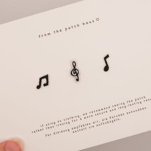 Peut inclure: Trois petits écussons brodés noirs en forme de notes de musique disposés horizontalement sur une carte blanche. La carte porte le texte from the patch haus avec un symbole de cœur et des instructions d'application en anglais et en allemand.