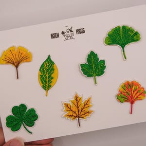 May include: A set of seven embroidered leaf patches arranged on a white card featuring the text PATCH HAUS with a small house icon. The collection includes various shapes and colours, such as a yellow ginkgo, a green clover, and a maple leaf.