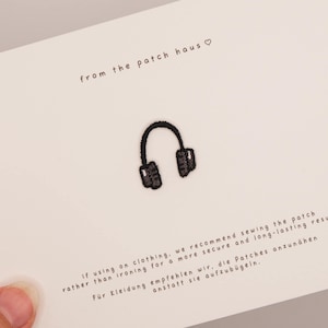 Könnte beinhalten: Ein kleiner schwarzer Stickaufnäher in Form von Kopfhörern, zentriert auf einer weißen Karte. Die Karte enthält den Text from the patch haus mit einem Herzsymbol sowie Anweisungen auf Englisch und Deutsch zum Annähen des Aufnähers.