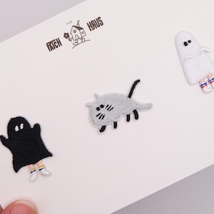 May include: Three embroidered patches on a white card featuring the text THE PATCH HAUS. The set includes a black ghost, a gray cat with black limbs, and a white ghost. Both ghosts wear white sneakers with red and blue striped socks.