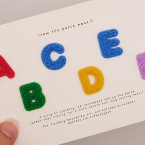 May include: A set of six colourful, textured letter patches labelled A through F, arranged on a white card. The letters are red, green, blue, yellow, blue, and purple. The card includes the text from the patch haus and sewing instructions.