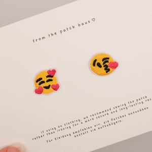 Könnte beinhalten: Zwei runde gestickte Aufnäher mit gelben Emoji-Gesichtern und rosa Herzen auf einer weißen Trägerkarte. Die Karte enthält den Text from the patch haus sowie Anweisungen auf Englisch und Deutsch zum Annähen der Aufnäher auf Kleidung.