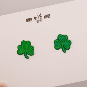 May include: Two embroidered shamrock patches in vibrant green thread, featuring a three-leaf clover design. The patches are attached to a white display card with the text THE PATCH HAUS and a small line-art illustration of a house.