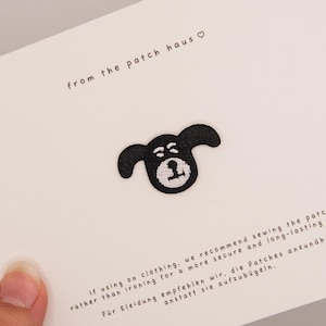 Puede incluir: Un parche bordado de cara de perro en blanco y negro centrado en una tarjeta blanca. La tarjeta presenta el texto from the patch haus con un símbolo de corazón en la parte superior e instrucciones sobre coser en lugar de planchar abajo.