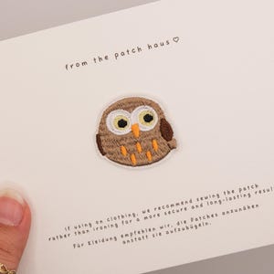 Pode incluir: Um emblema bordado de coruja com fios castanhos, brancos e cor de laranja, centrado num cartão branco com o texto from the patch haus e instruções para coser o emblema na roupa para um resultado seguro e duradouro.