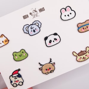 Op de afbeelding: Een verzameling van negen kleine geborduurde patches met cartoon-dierengezichten, waaronder een kat, koala, panda, konijn, beer, kikker, hert en een figuurtje met een kerstmuts, met de tekst THE PATCH HAUS bovenaan in het midden.