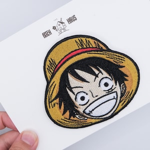 May include: An embroidered patch featuring a cartoon character with black hair and a wide smile, wearing a yellow straw hat with a red band. The patch is displayed on a white card with the text THE PATCH HAUS and a small house icon printed above.