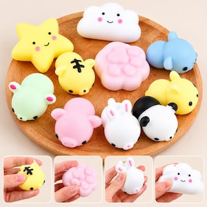 May include: A collection of small, soft, squishy silicone toys in various shapes including a yellow star, white cloud, pink paw print, blue animal, green pig, yellow tiger, pink pig, white rabbit, and black and white panda on a wooden tray.
