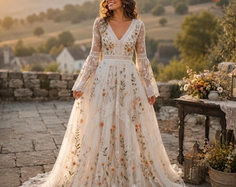 Puede incluir: Un vestido blanco hasta el suelo con escote en V, mangas largas acampanadas y un intrincado bordado floral en tonos naranja, amarillo y verde. El vestido está confeccionado en tela transparente con detalles de encaje en la cintura.