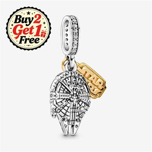 May include: A silver-coloured charm shaped like the Millennium Falcon spaceship with intricate mechanical detailing. The bail is encrusted with small clear stones. A separate gold-coloured rectangular tag hangs from the bail, featuring the embossed text STAR WARS.