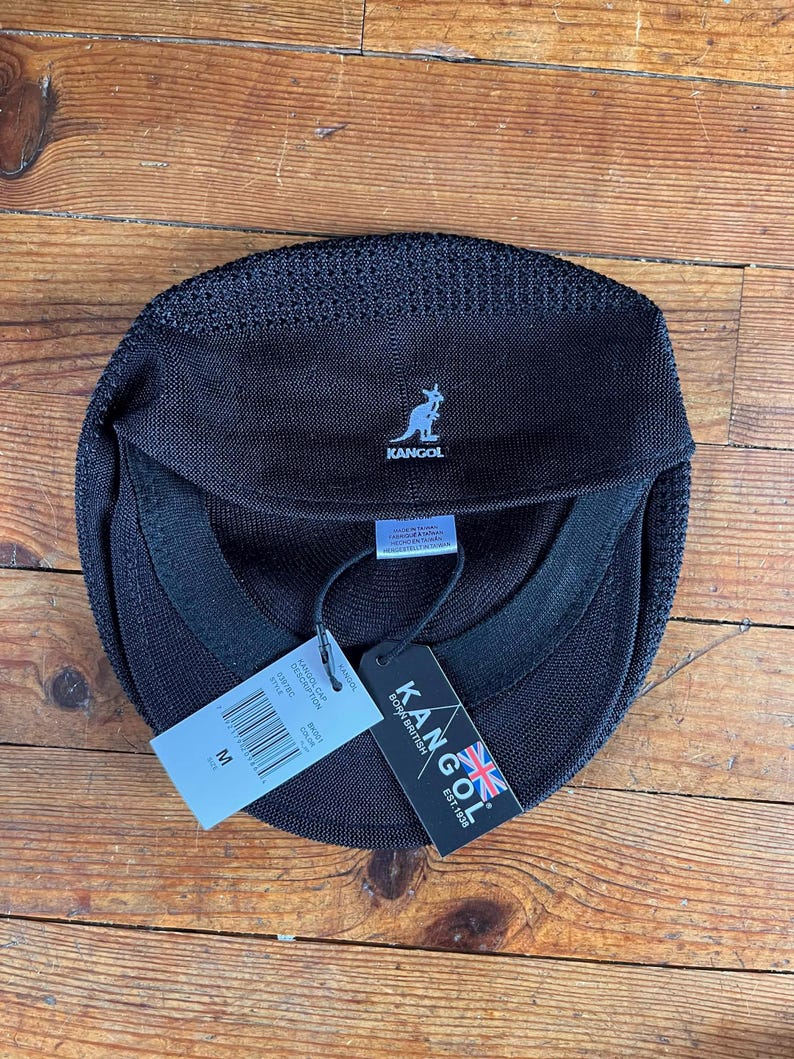 Pu&ograve; includere: Un berretto Kangol nero con finitura in maglia testurizzata e un logo a canguro azzurro ricamato sul davanti. Il berretto presenta una fascia interna, un'etichetta di manutenzione bianca e due cartellini di carta, uno dei quali indica la taglia M.