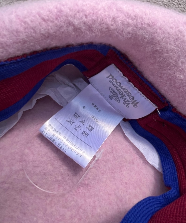 Puede incluir: Un sombrero de fieltro rosa claro con una etiqueta interior blanca que muestra el logotipo y el texto de Vivienne Westwood. La banda interior est&aacute; forrada con una tela a rayas azul brillante y rojo oscuro. Etiqueta de 100% lana.