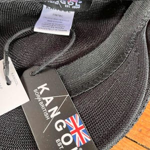 Pu&ograve; includere: Un berretto nero Kangol Tropic 504 Ventair in tessuto a rete testurizzato. L'interno include un'etichetta di manutenzione bianca con la taglia medium e un cartellino nero con il testo Kangol Born British Est. 1938 e una bandiera britannica.