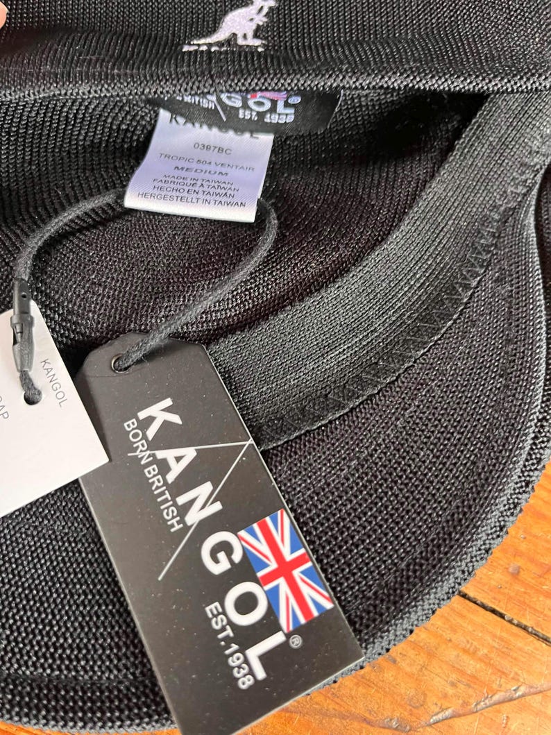 Pu&ograve; includere: Un berretto nero Kangol Tropic 504 Ventair in tessuto a rete testurizzato. L'interno include un'etichetta di manutenzione bianca con la taglia medium e un cartellino nero con il testo Kangol Born British Est. 1938 e una bandiera britannica.