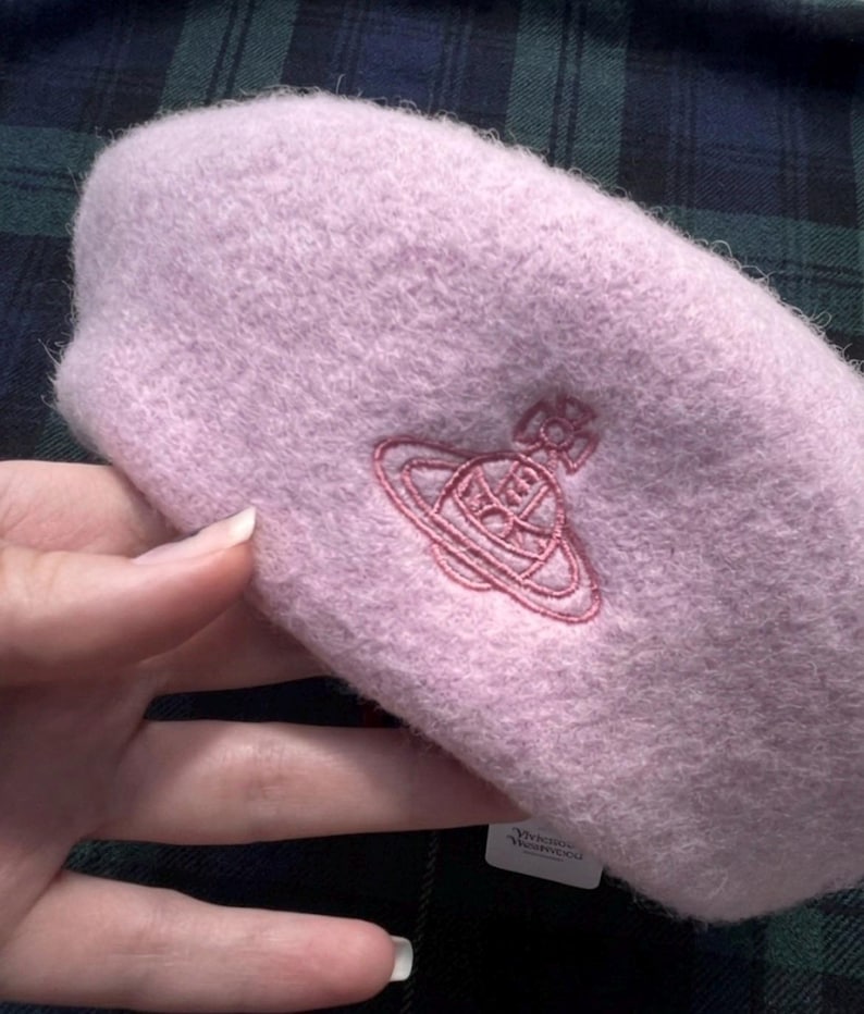 Puede incluir: Una boina suave y esponjosa de color rosa claro con un logotipo de orbe de Vivienne Westwood bordado en rosa m&aacute;s oscuro en la parte delantera. El gorro tiene una apariencia texturizada similar a la lana e incluye una etiqueta blanca.