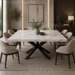 May include: A square dining table with a white marble top featuring grey veining and a black metal X-shaped base. Eight upholstered beige armchairs with black legs are arranged around the table. A grey vase with green foliage sits in the centre.