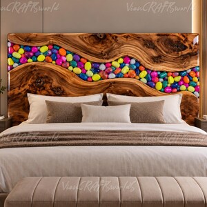 May include: A rectangular headboard featuring a natural wood grain finish with a central, winding river-like inlay filled with smooth, multi-colored polished stones in shades of bright pink, yellow, blue, orange, and green, set against a bed.