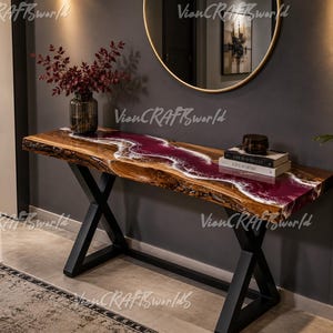 May include: A live edge wood console table featuring a central river design made of deep burgundy resin with white swirling accents. The table is supported by two black metal X-shaped legs and holds a glass vase with red foliage and two stacked books.