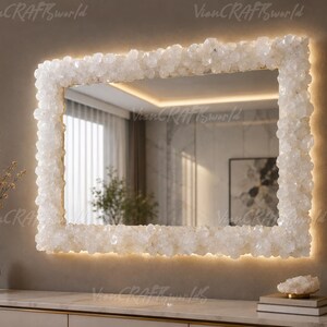 May include: A rectangular wall mirror featuring a thick frame encrusted with numerous white, translucent, crystalline rock formations. The mirror is illuminated from behind by a warm, soft LED light that creates a glowing halo effect around the edges.