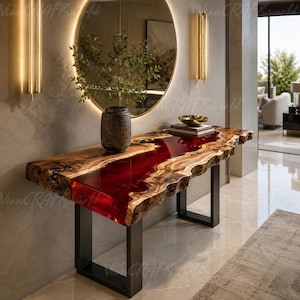 May include: A rectangular console table featuring a live-edge wood slab with a central, translucent deep red resin river inlay. The table is supported by two black metal U-shaped legs and holds a dark textured vase with greenery and a small bowl.