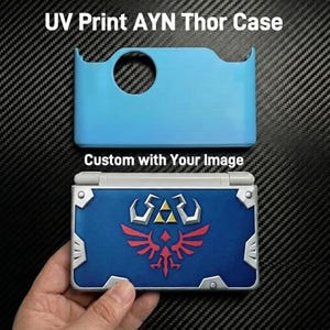 May include: A light blue protective case for the AYN Thor handheld console with a circular cutout, positioned above a closed handheld console featuring a blue cover with a red and silver winged crest emblem and silver corner accents. Text reads UV Print AYN Thor Case and Custom with Your Image.