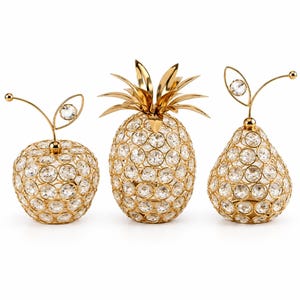 May include: Three decorative fruit sculptures shaped like an apple, a pineapple, and a pear. Each piece is constructed from a gold-toned metal wire frame embedded with numerous clear, round faceted crystals that catch the light.