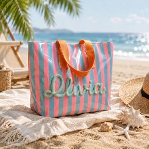 Può includere: Una borsa tote con strisce verticali rosa e azzurre e due manici in tessuto arancione. Il nome Olivia è scritto sulla parte anteriore in un carattere corsivo verde chiaro in rilievo e testurizzato. La borsa ha una finitura lucida.