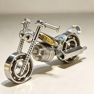 以下が含まれることがあります： 銀色の金属部品で作られたミニチュアのオートバイの彫刻。車輪にはボールベアリング、エンジンにはコイル状のスプリング、ヘッドライト部分にはナットが使用されており、フレームには小さな真鍮色のアクセントパーツが取り付けられています。