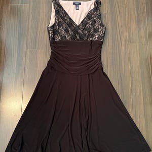 May include: A sleeveless knee-length dress featuring a black lace bodice overlay with a V-neckline over a beige lining. The waist is gathered with horizontal ruching, transitioning into a solid black flared skirt. The label reads Chaps.
