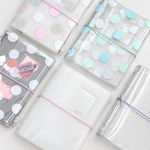 Puede incluir: Cinco fundas de plástico transparente para cuadernos con varios patrones de lunares y bandas elásticas de colores. Cada funda incluye un pequeño bolsillo transparente en la parte frontal. Los diseños incluyen lunares grandes rosas, blancos, grises, azules y verdes.