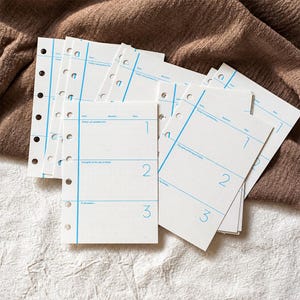 May include: A stack of white planner refill pages with six punched holes along the left edge. Each page features blue printed lines, the text 'Today I am grateful for...', 'Thoughts of the day & Notes', 'To be better...', and the numbers 1, 2, and 3.