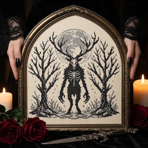 Peut inclure: Une broderie au point de croix dans un cadre doré arqué de style gothique. Le motif représente une créature noire, squelettique et boisée, debout entre deux arbres dénudés devant une grande lune grise circulaire sur un tissu crème.