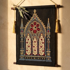 May include: A black fabric wall hanging featuring a detailed cross-stitch design of a gothic cathedral window with red roses, blue architectural accents, and gold detailing. The piece is suspended from a dark wooden rod with gold tassels and cord.