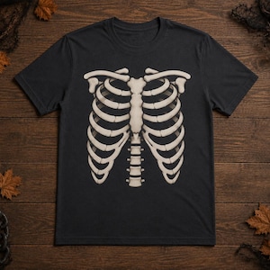 May include: A black short-sleeved t-shirt featuring a centered, off-white graphic print of a human rib cage and sternum. The skeletal illustration displays the individual ribs curving outward from the central bone structure in a detailed design.