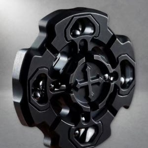 Puede incluir: Un fidget spinner de metal negro mate con un diseño simétrico tipo engranaje de cuatro brazos. El centro del spinner muestra un emblema de cruz en relieve, y cada brazo contiene un recorte circular con rodamientos de bolas metálicos visibles.