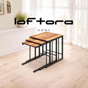 Könnte beinhalten: Ein Set aus drei Satztischen mit rechteckigen Holzplatten mit natürlicher Maserung und schwarzen Metallrahmen. Der Text loftora HOME ist über den Tischen zu sehen. Die Tische sind in einer kaskadierenden, gestuften Formation angeordnet.