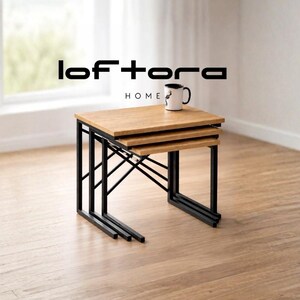 May include: A set of three nested tables with light brown wooden tops and black metal frames. The tables are stacked together, and a white mug with a black handle sits on the largest top surface. The text lof tora HOME is visible above.