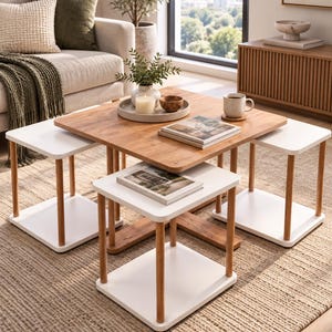May include: A nesting table set featuring a large square wooden table with a natural grain finish and three smaller square white tables with four cylindrical wooden legs each. The tables are arranged to fit together in a compact configuration.