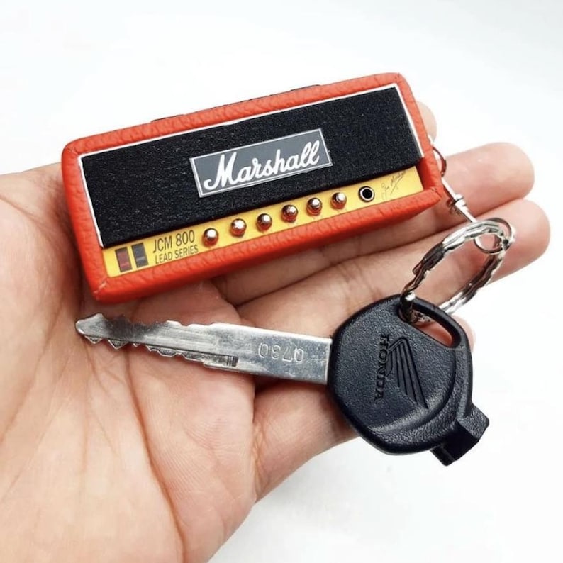 May include: A rectangular orange and black keychain shaped like a Marshall JCM 800 Lead Series amplifier head, featuring a silver Marshall logo, gold-colored control knobs, and a metal ring attached to a black Honda car key with a silver blade.