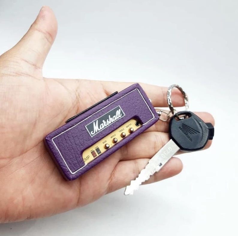 May include: A purple rectangular keychain designed to resemble a Marshall guitar amplifier, featuring the white Marshall logo, control knobs, and a silver metal ring attached to a black Honda motorcycle key with a silver metal blade.