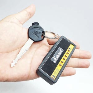 May include: A metal Honda vehicle key attached to a rectangular keychain shaped like a Marshall JCM 800 Lead Series guitar amplifier head. The keychain features a black textured front panel with the white Marshall logo and gold control knobs.