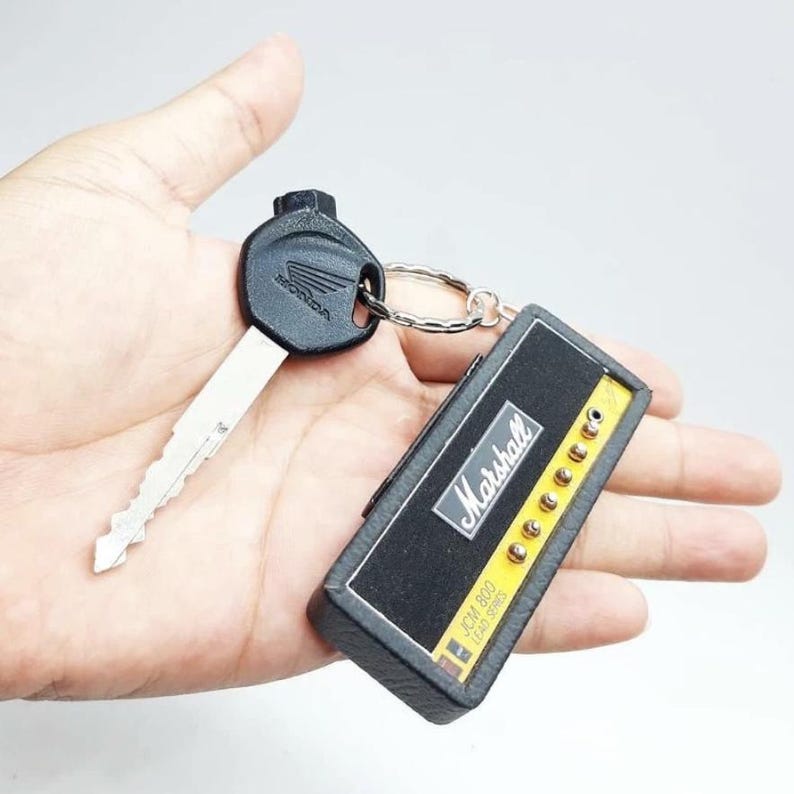 May include: A metal Honda vehicle key attached to a rectangular keychain shaped like a Marshall JCM 800 Lead Series guitar amplifier head. The keychain features a black textured front panel with the white Marshall logo and gold control knobs.